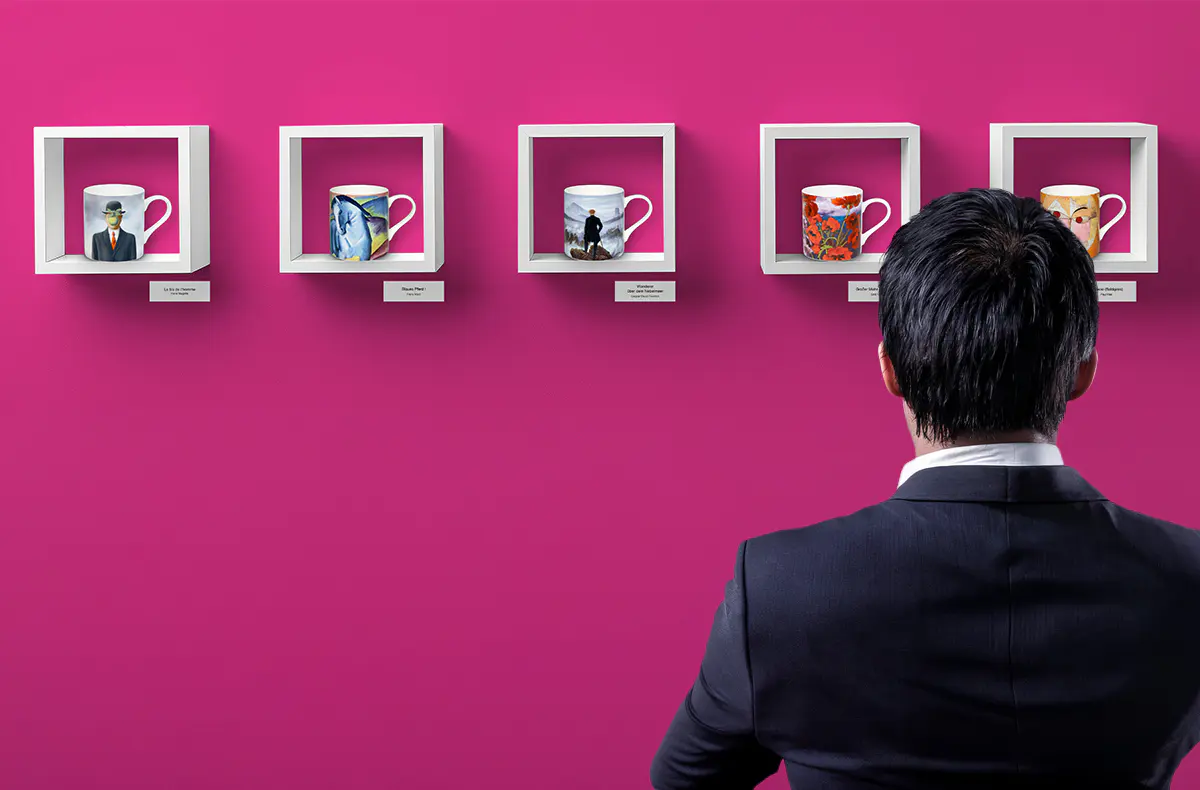 A visitor admiring KÖNITZ ARTselection mugs displayed like paintings in white frames on a pink gallery wall